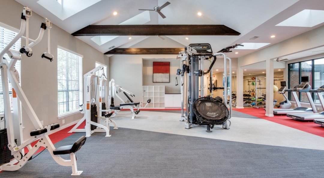 a gym room with a red carpet and white walls at The Hyde Park at Valley Ranch